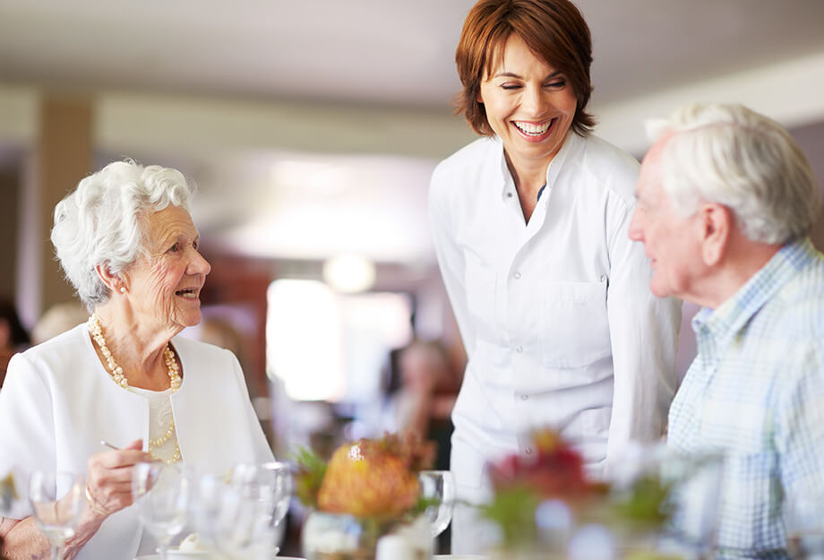 Caretaker interacting with seniors during a meal at a community dining area.