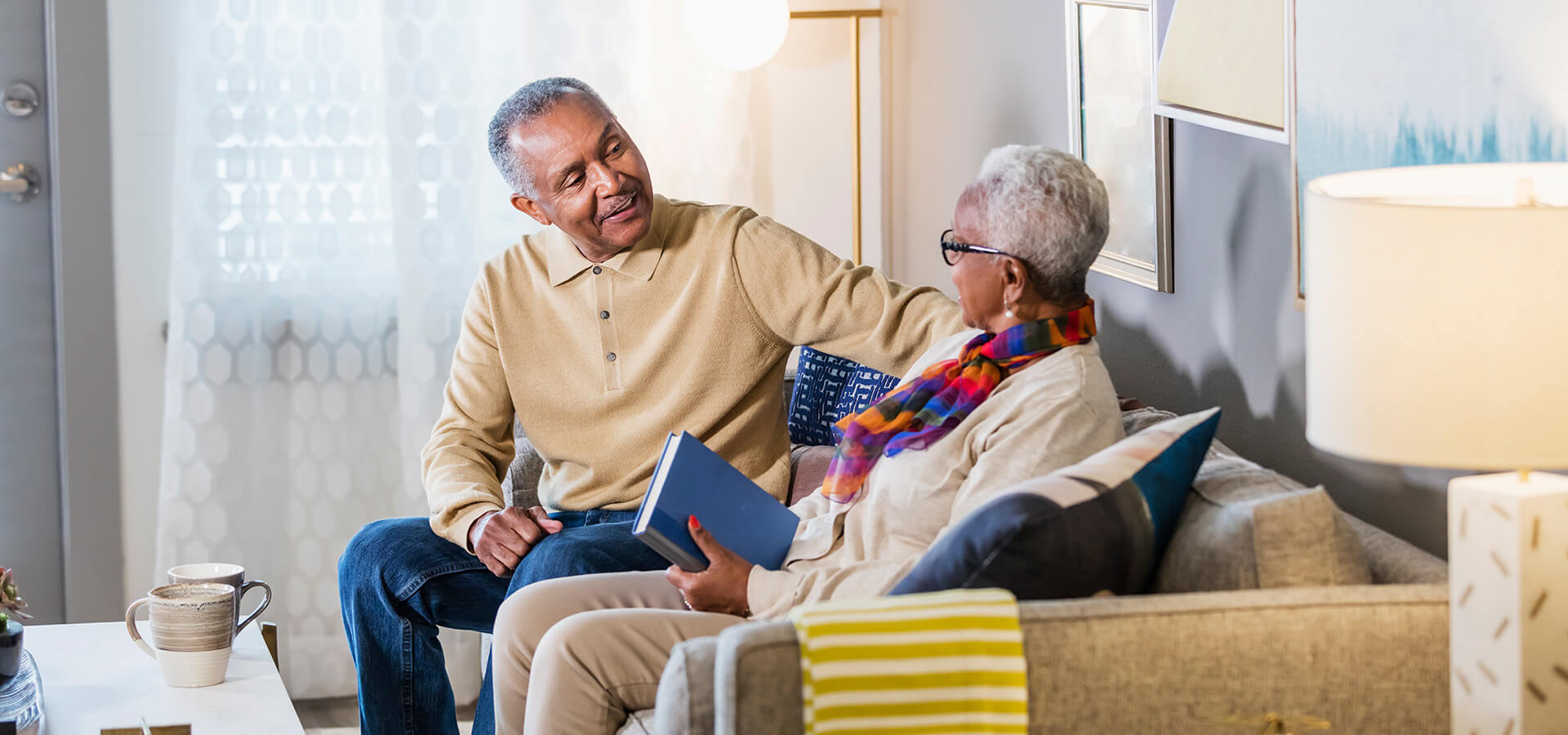 Elderly couple enjoying conversation in a cozy living unit with warm lighting.