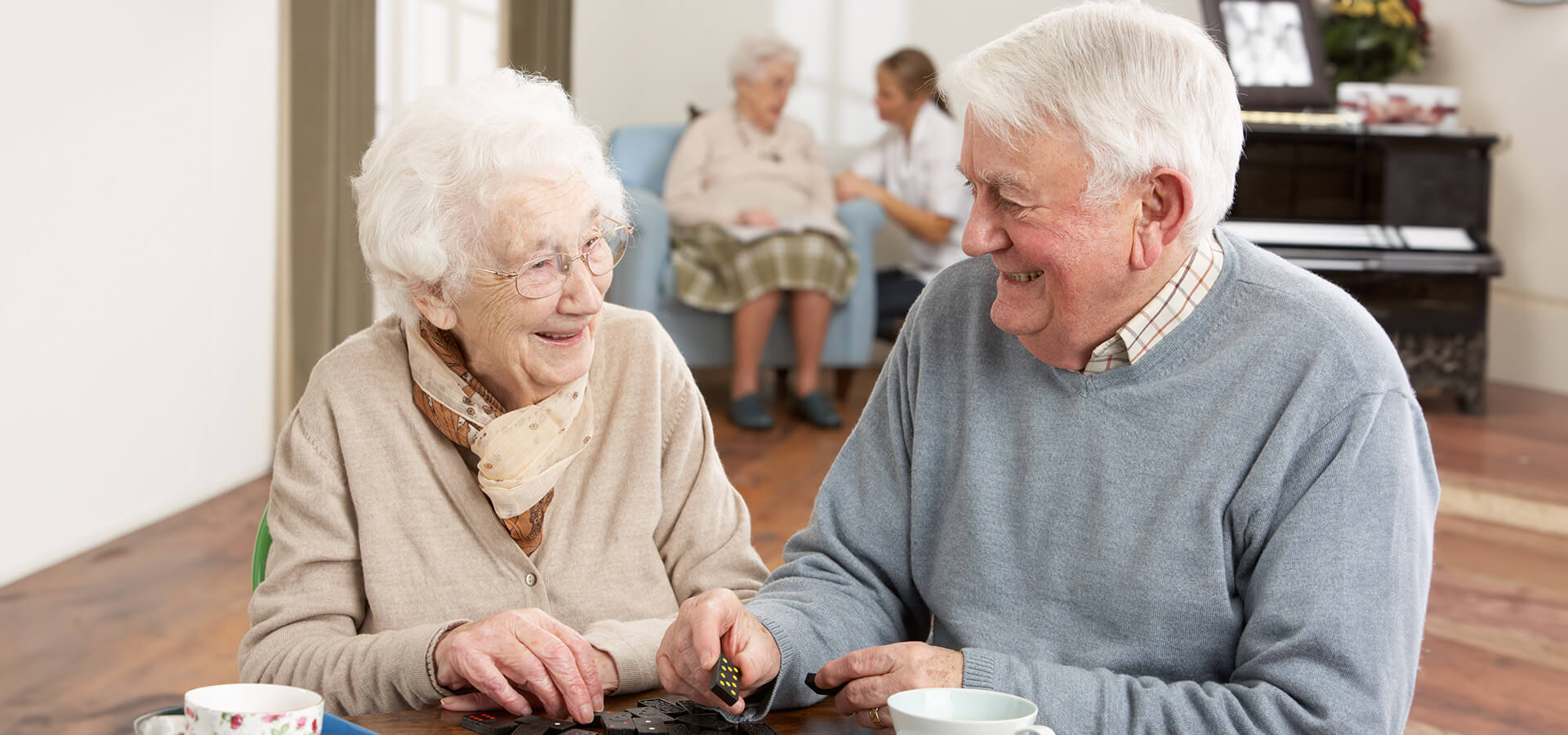 Two seniors smiling and playing dominoes at living community unit.