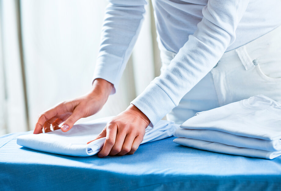 Person in white outfit folding clothes on a blue table in a unit.