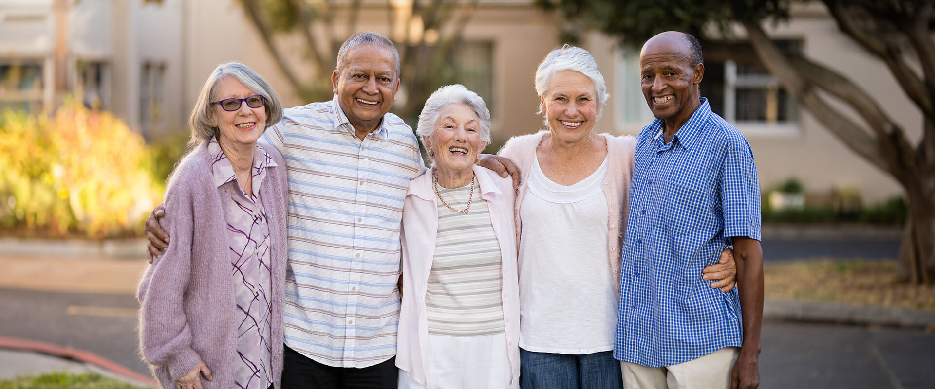 Group of smiling seniors standing outdoors in a residential community setting.