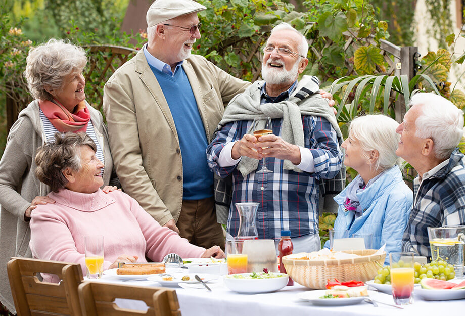 Group of seniors enjoying an outdoor meal, laughing and socializing in a garden setting.