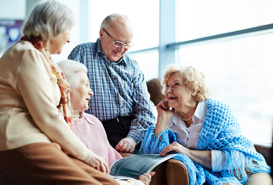 Four older adults smiling and sitting together in a bright, open community space.