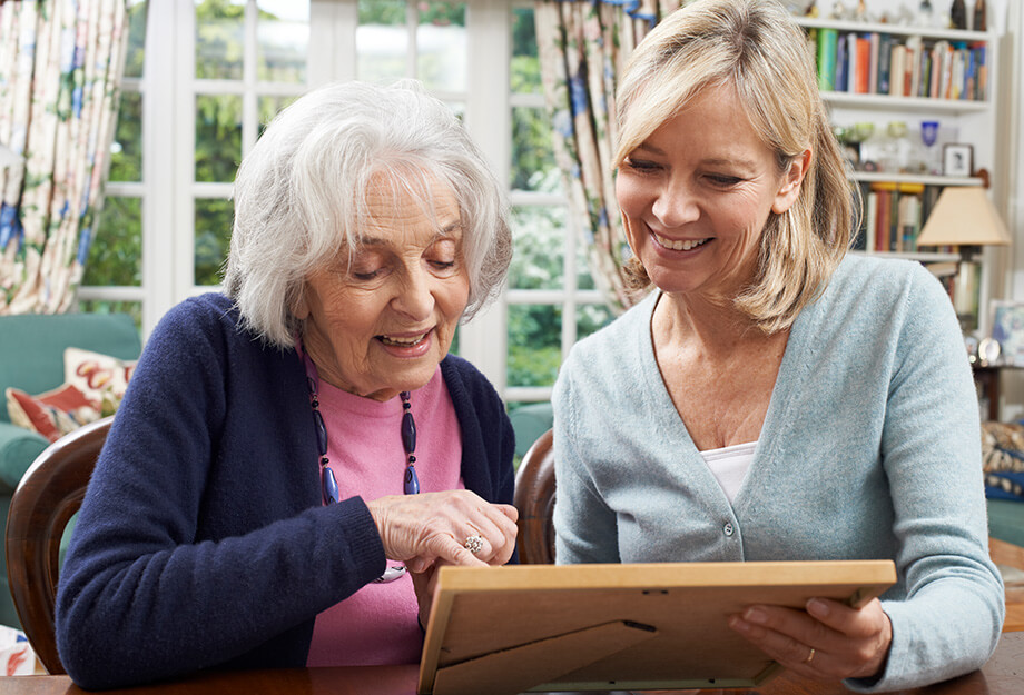 Two women enjoying a framed photograph in a cozy living space with books and plants.