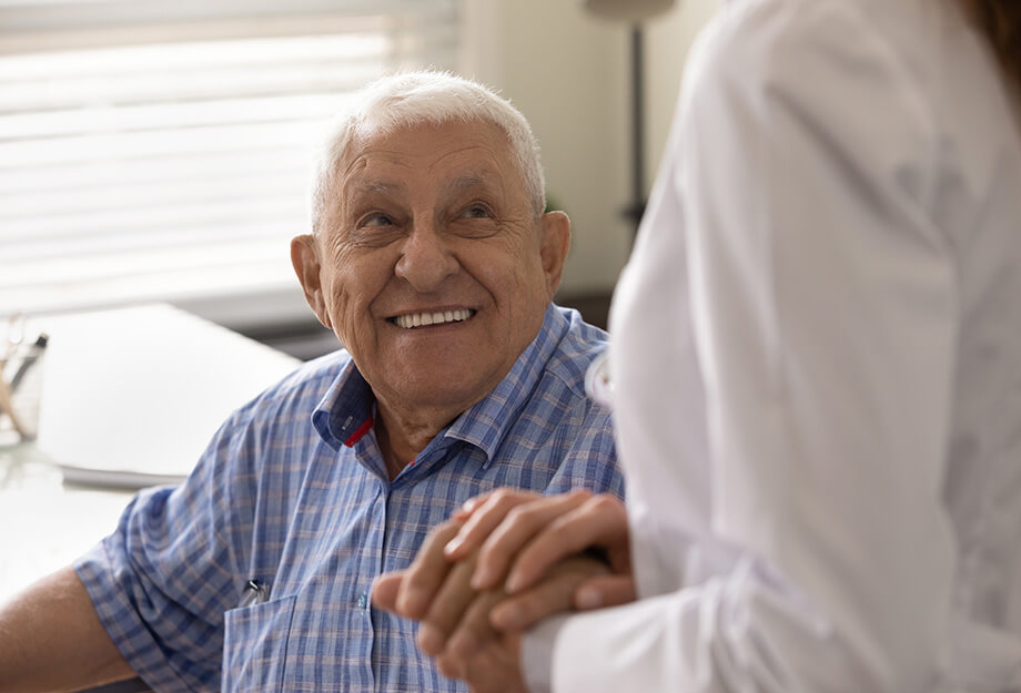 Elderly man smiling and holding hands in a bright room.